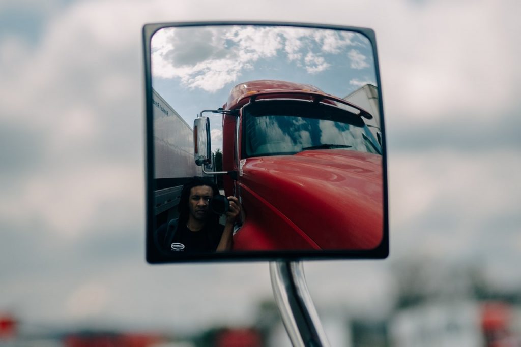 A man captures a selfie in a truck's rearview mirror, highlighting the importance of safety in commercial driving.