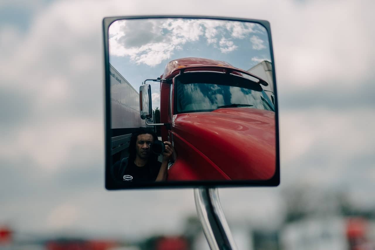 A man captures a selfie in a truck's rearview mirror, highlighting the importance of safety in commercial driving.