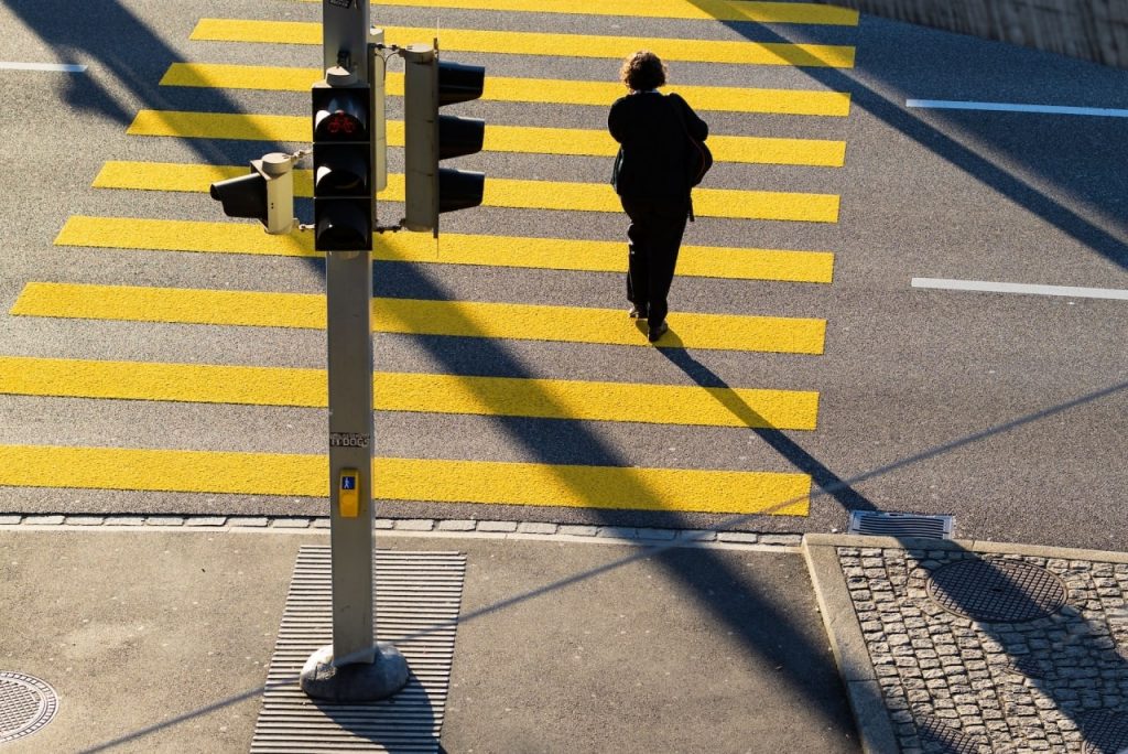 A woman in black clothing crosses a street at a marked crosswalk in Rancho Cucamonga, highlighting pedestrian safety concerns.