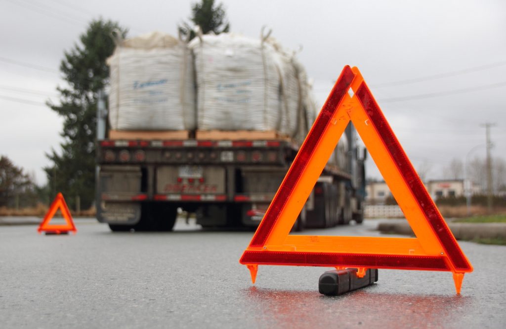 A truck navigating a road, accompanied by a warning sign highlighting the dangers of blindspots and potential accidents.