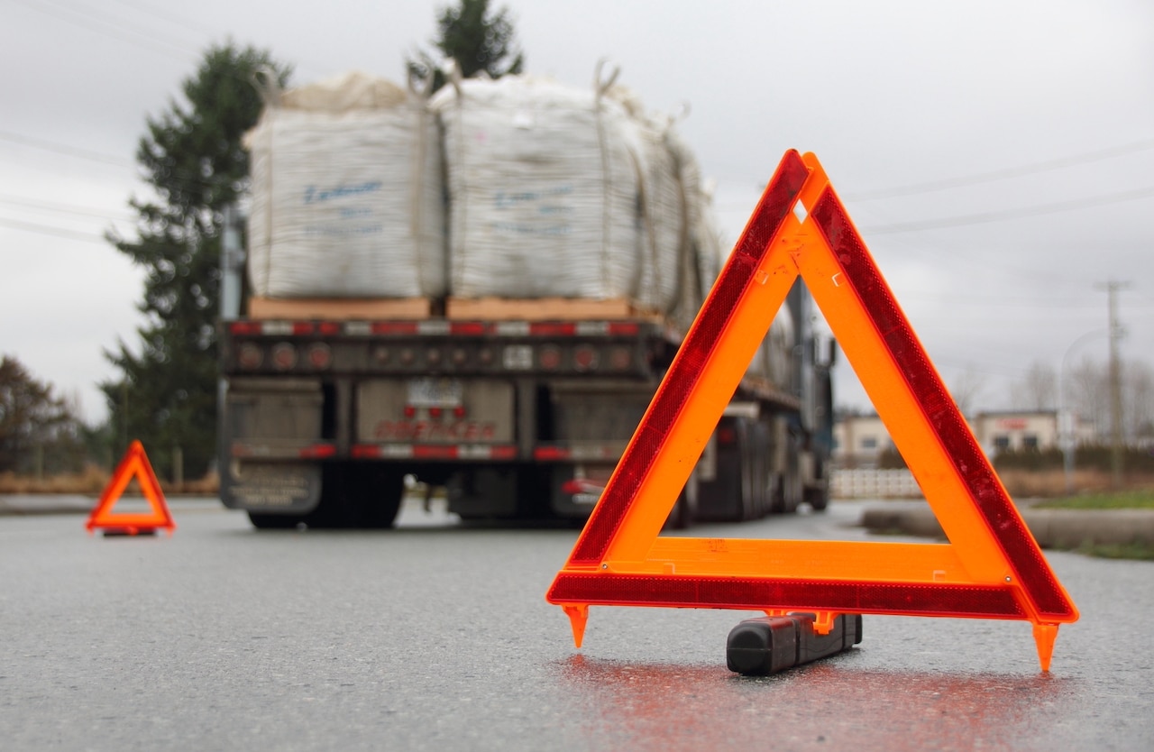 A truck navigating a road, accompanied by a warning sign highlighting the dangers of blindspots and potential accidents.