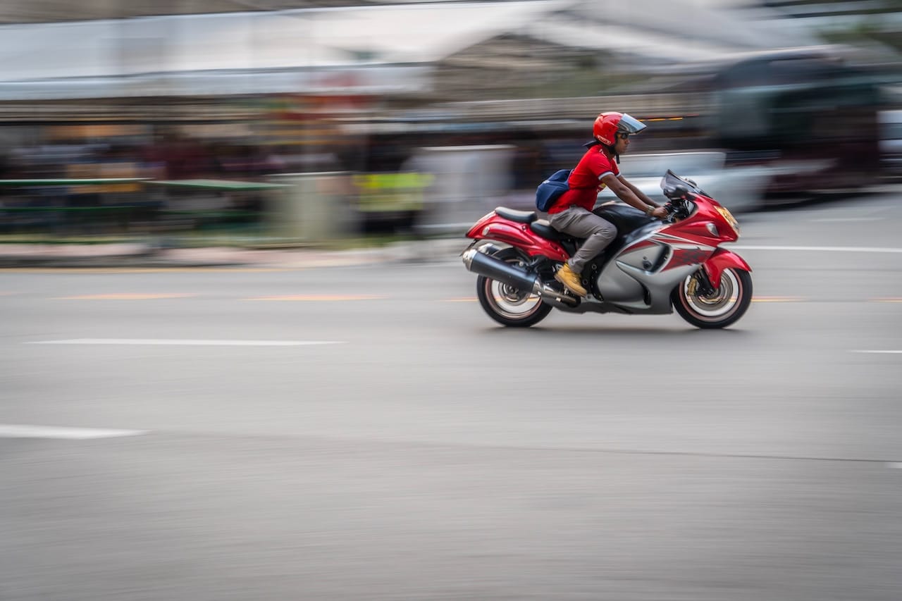 A person rides a red motorcycle through a city street, highlighting the risks of motorcycle accidents in Rancho Cucamonga.