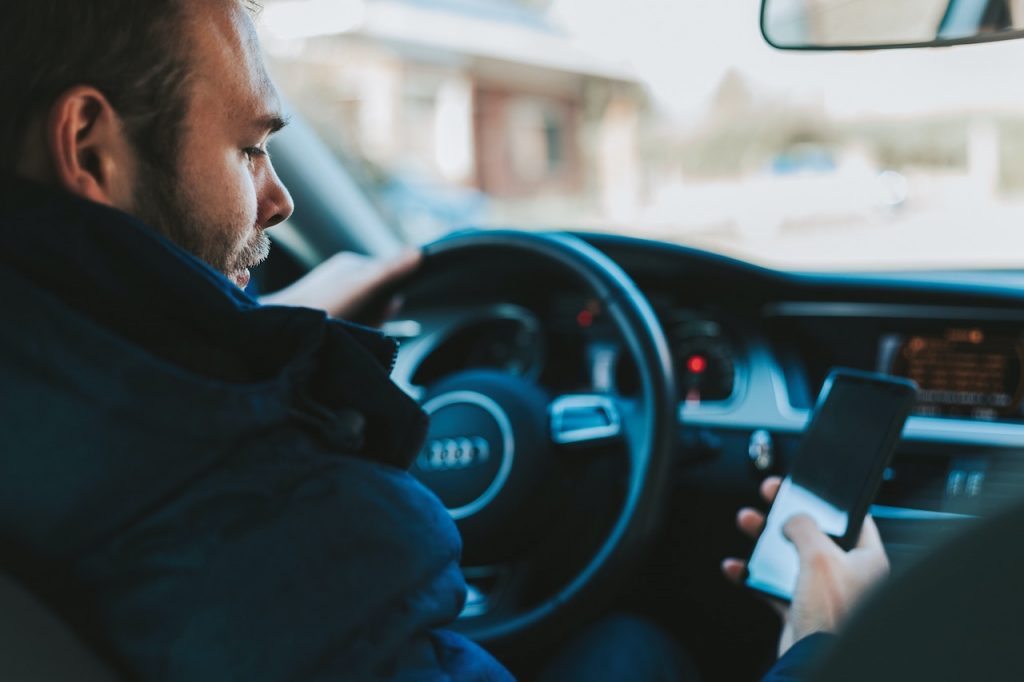 A man in the driver's seat of a car, distracted by his cell phone, highlighting the dangers of distracted driving.