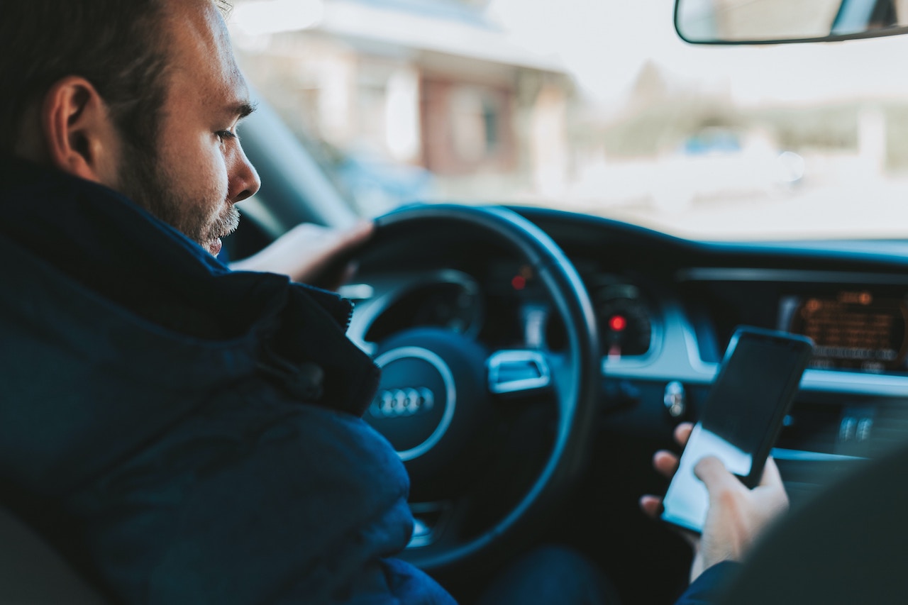 A man in the driver's seat of a car, distracted by his cell phone, highlighting the dangers of distracted driving.